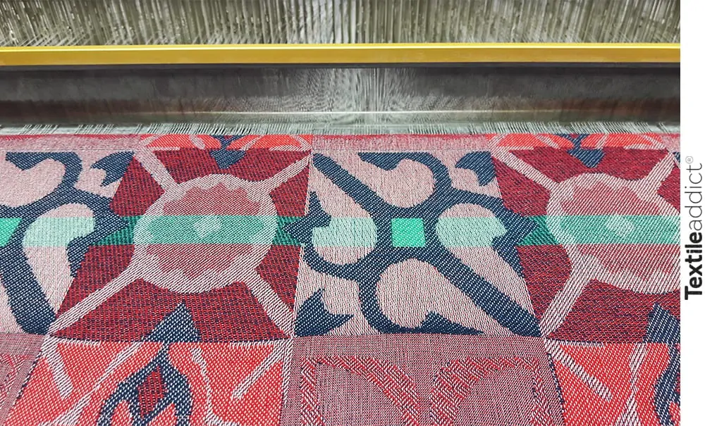 Illustration d’un métier à tisser Jacquard en action, produisant une étoffe façonnée avec un motif géométrique complexe. Cette image met en lumière le processus de tissage, de la mise en carte à la production, soulignant l’expertise du designer textile dans la création de tissus pour la mode et l’ameublement.